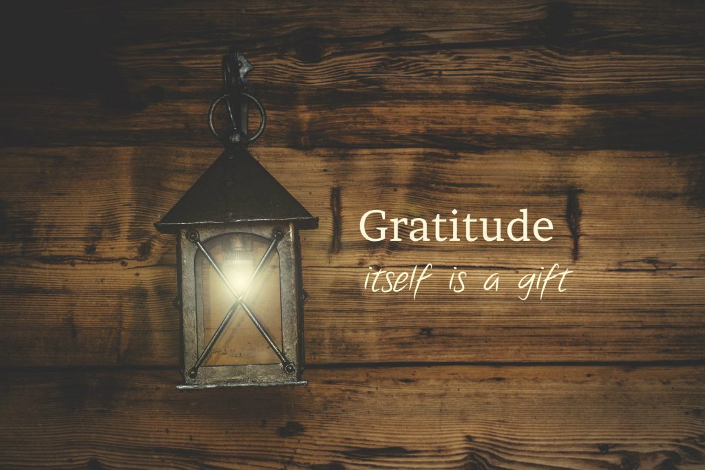 Gratitude itself is a gift. Lettering on wood beside a lit lantern