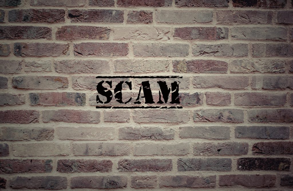 "Scam" on brick wall on scammed blog about the trauma triggered by scamming